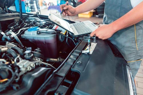 A man is working on the engine of a car with a laptop.