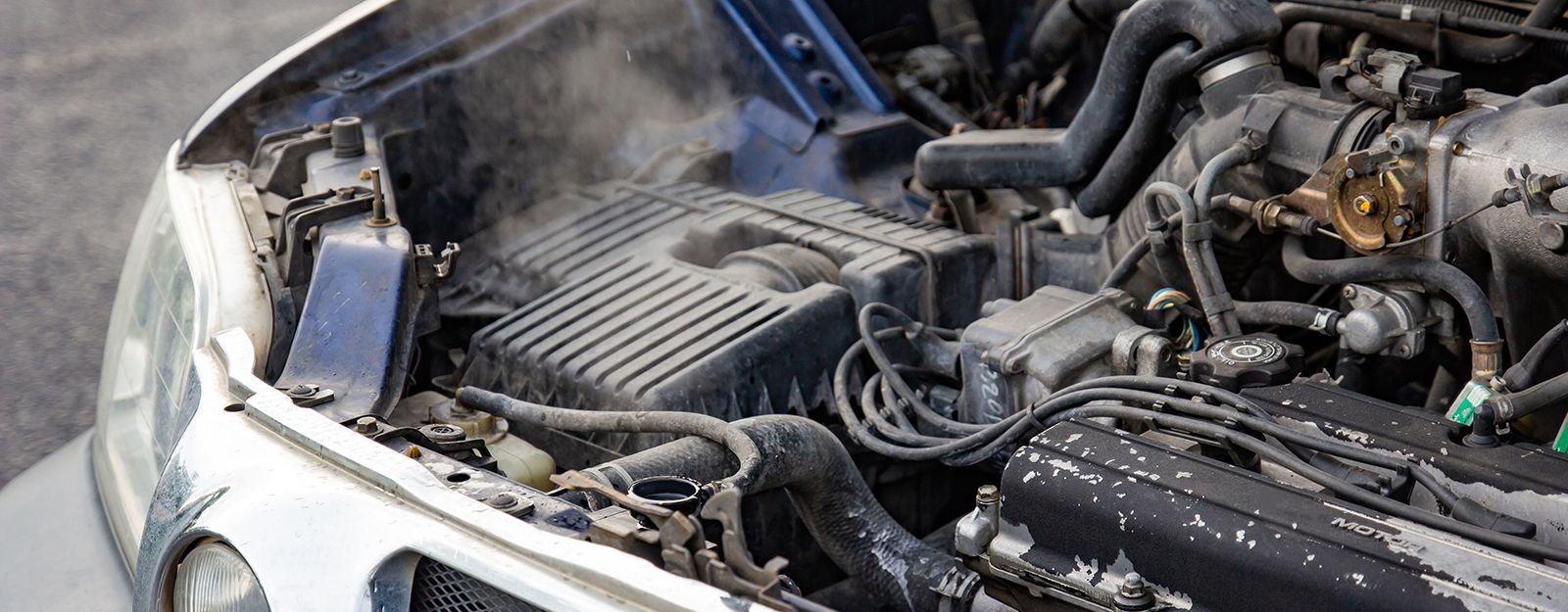 Car engine overheating, steam rising from under the hood.