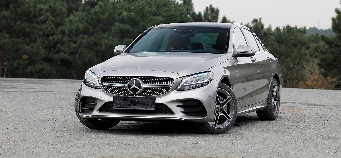 Silver Mercedes-Benz C-Class sedan parked on gravel with trees in the background.