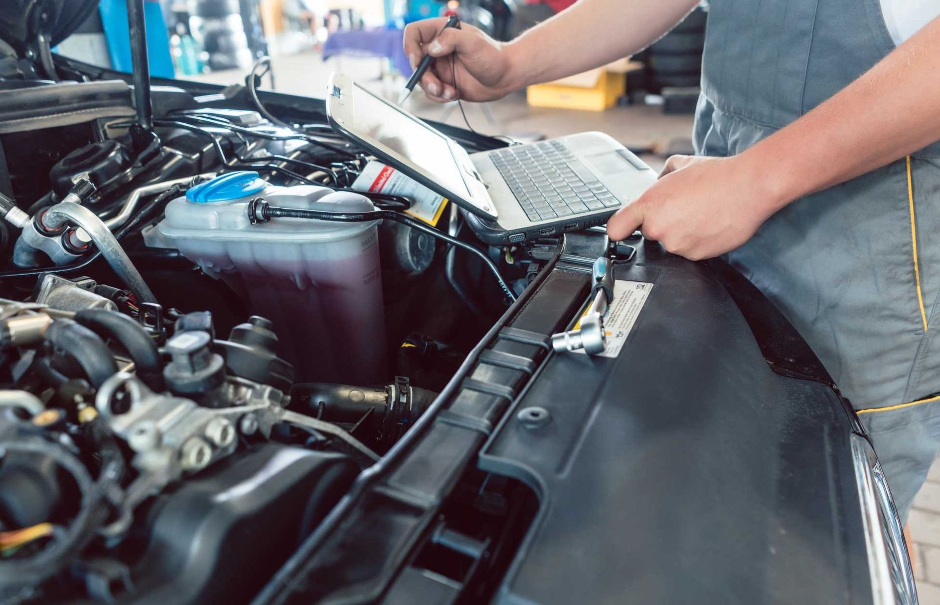 A man is working on a car engine with a laptop.