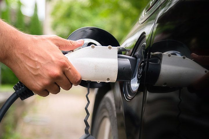 Multicultural person plugging in an electric vehicle charger into a black car's charging port, demonstrating eco-friendly EV charging technology.