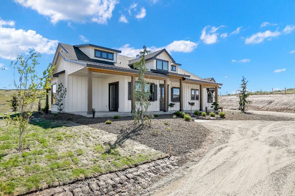 A large white house is sitting on top of a dirt road.