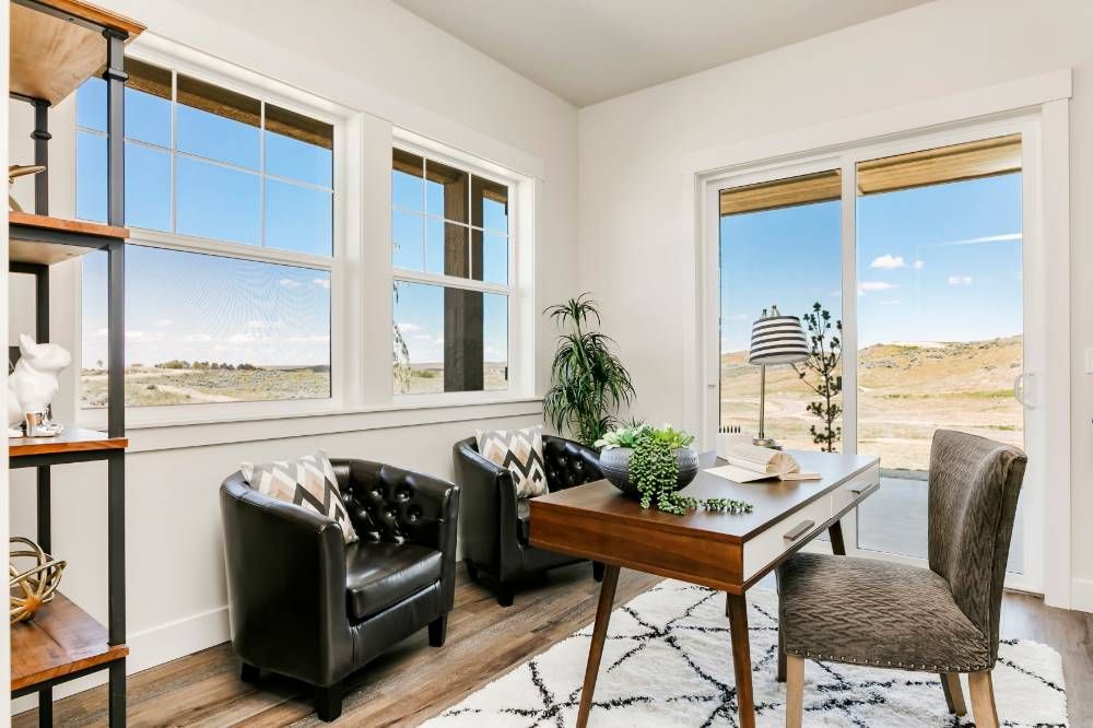 A home office with a desk , chairs , and a large window.