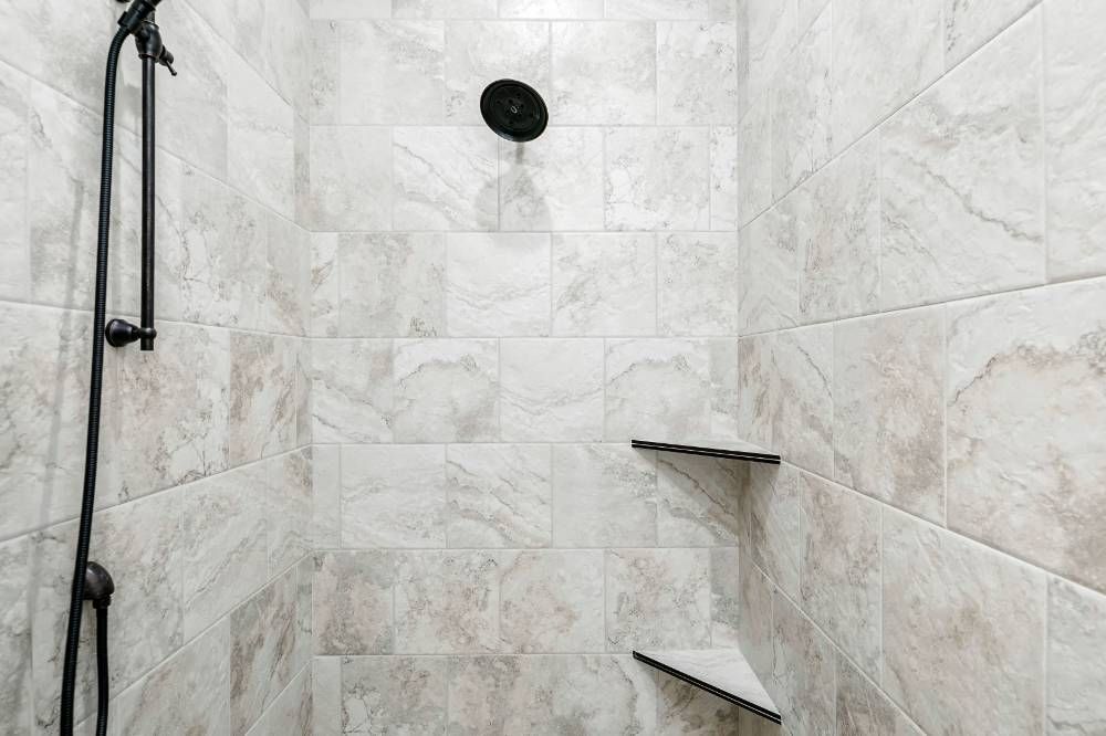 A shower with a black shower head and a shelf.
