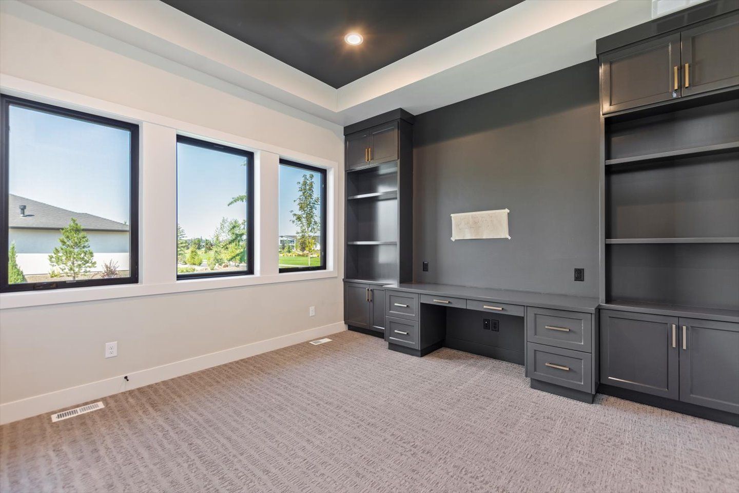 An empty room with a desk , shelves , and windows.
