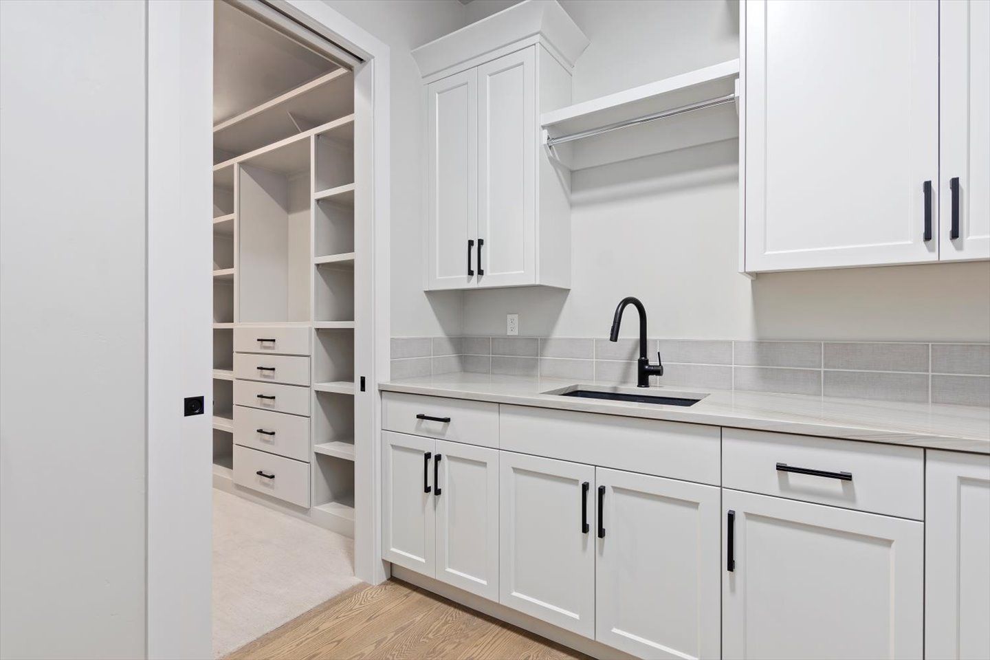 A laundry room with white cabinets , a sink , and a walk in closet.