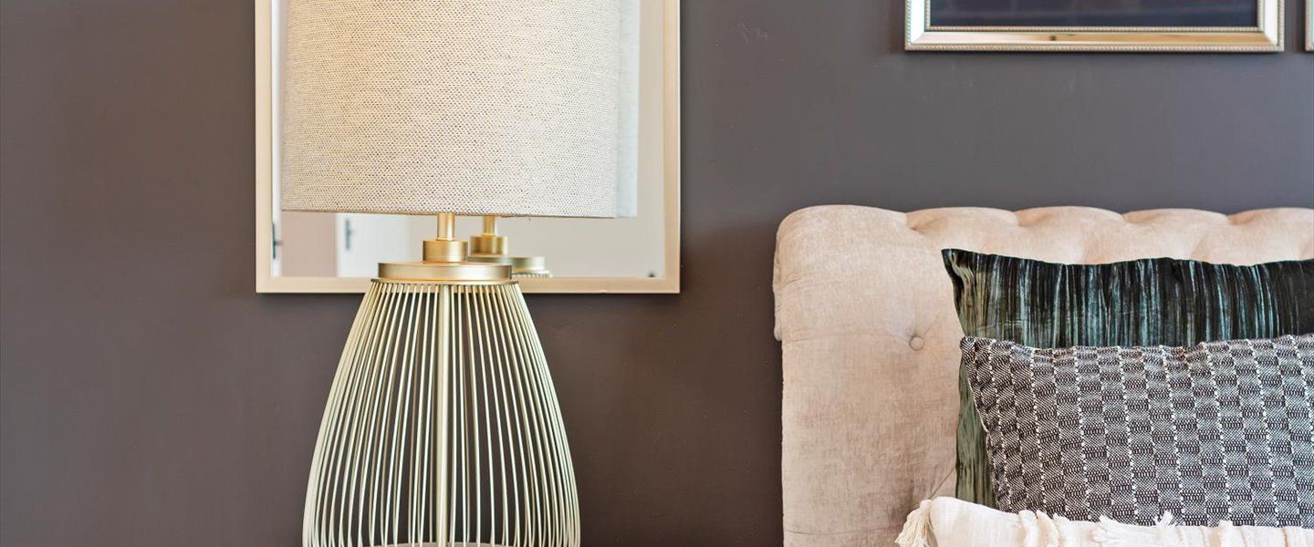 A bedroom with a bed , lamp , mirror and pillows.