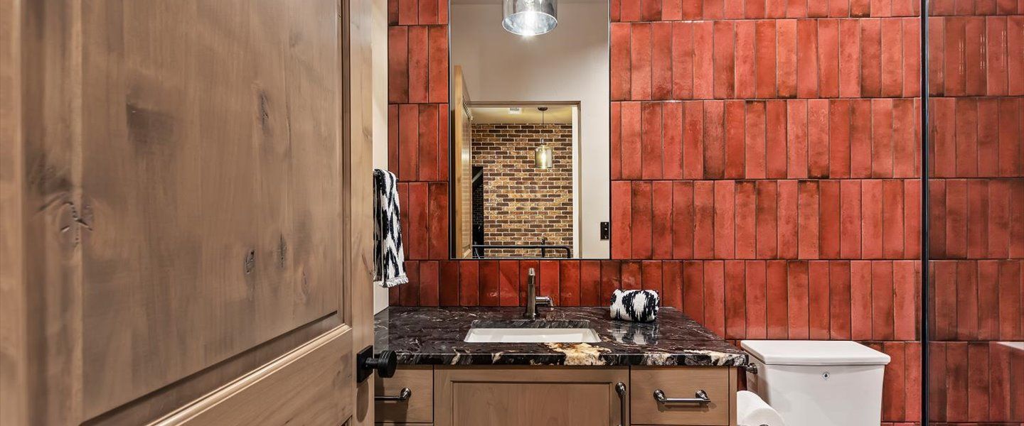 A bathroom with a sink , toilet , mirror and red tiles.