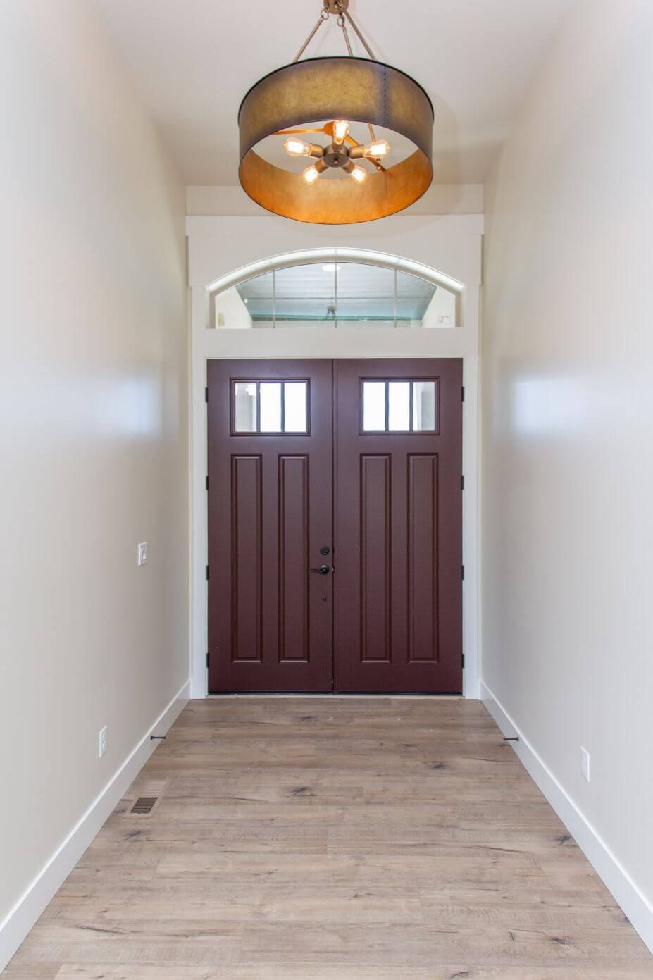 A hallway with a red door and a chandelier hanging from the ceiling.