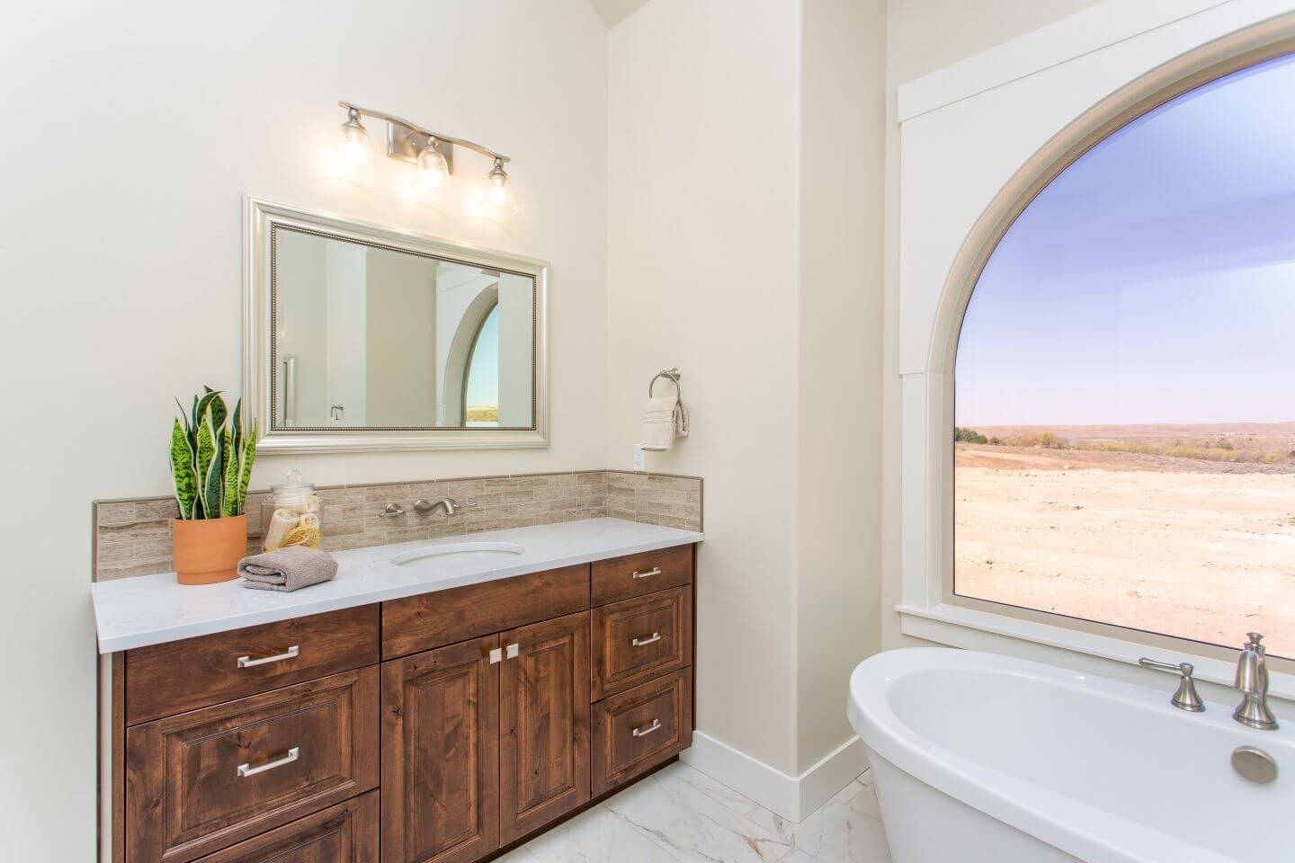 A bathroom with a tub , sink , mirror and window.