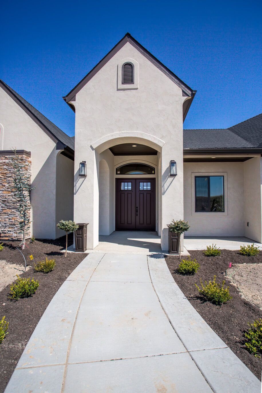 A white house with a brown door and a concrete walkway leading to it.