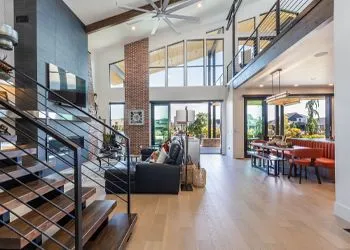 A large white house with a porch and a lot of windows is sitting on top of a dirt field.