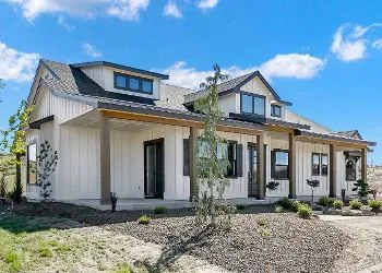 A large white house with a porch and a lot of windows is sitting on top of a dirt field.