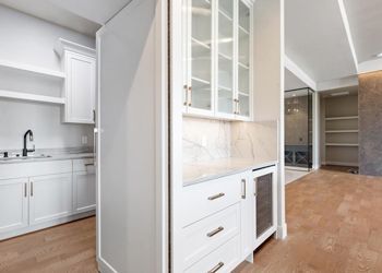 A kitchen with white cabinets , granite counter tops , and a wine cooler.