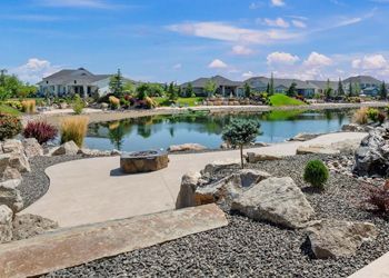 A large pond surrounded by rocks and gravel with houses in the background.