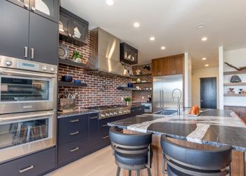 A kitchen with black cabinets and stainless steel appliances and a brick wall.