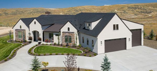 A large white house with a black roof is sitting on top of a lush green hillside.