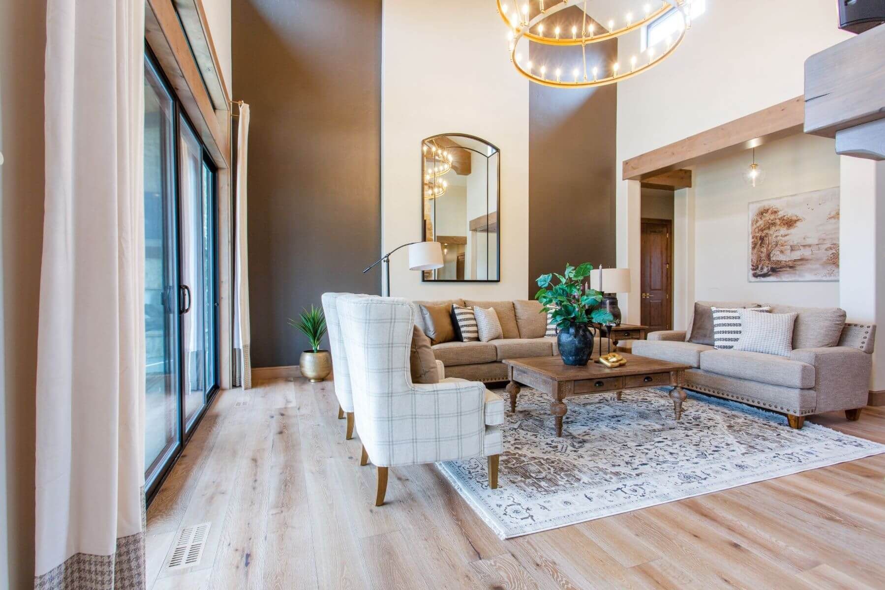Spacious living room with tan and brown tones. Sliding glass doors, large mirror, and a chandelier.