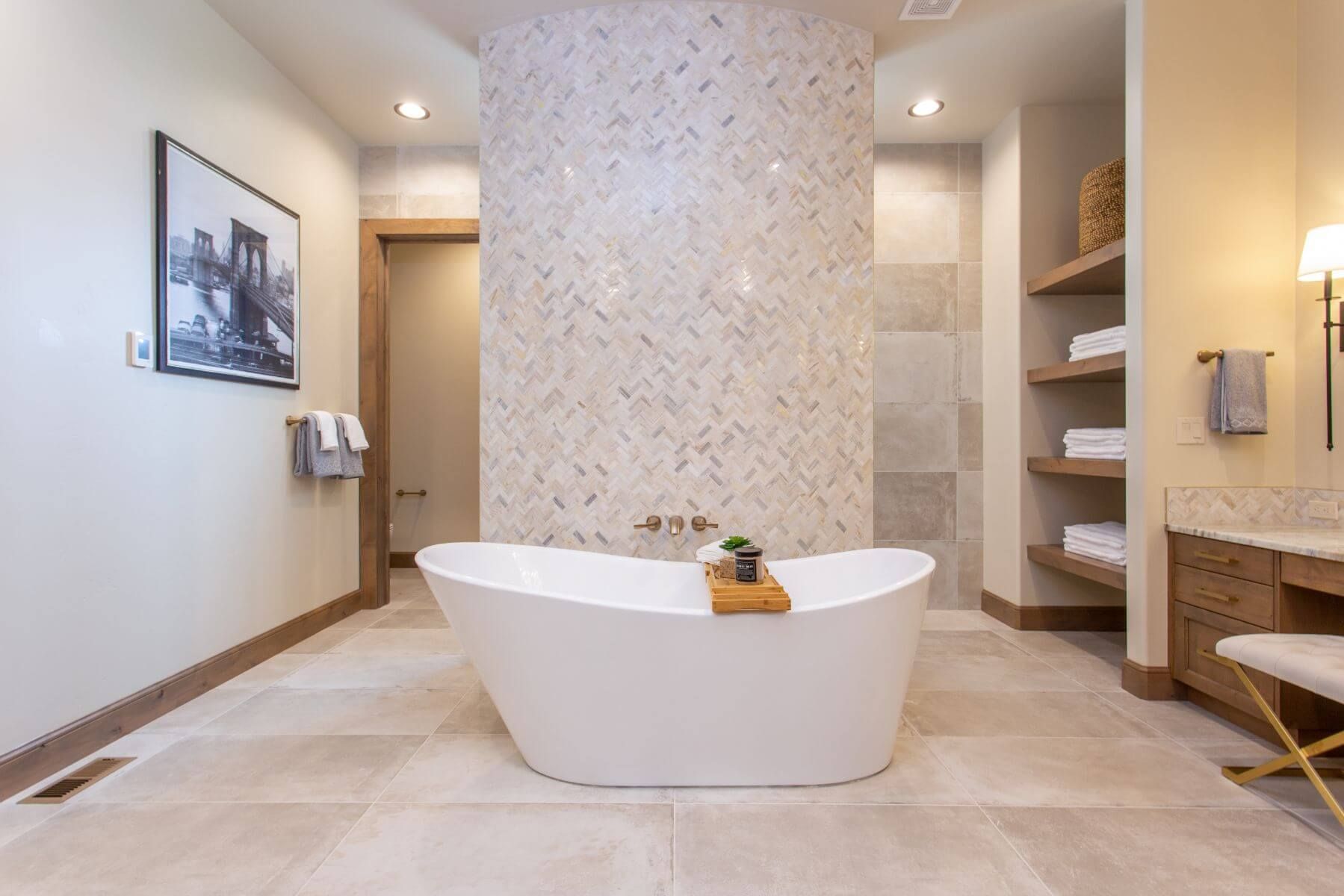 A modern bathroom with a freestanding tub, tiled feature wall, shelving, and vanity.