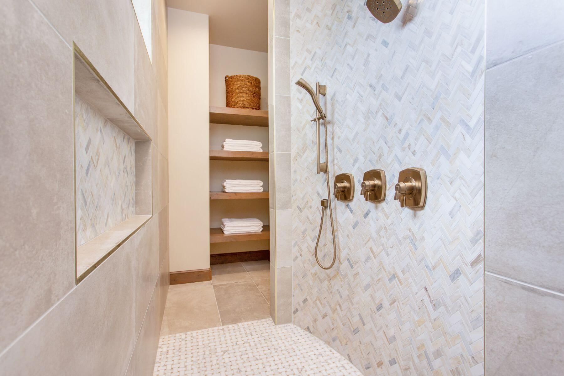 Modern bathroom with patterned shower tile, gold fixtures, and built-in shelves for towels.