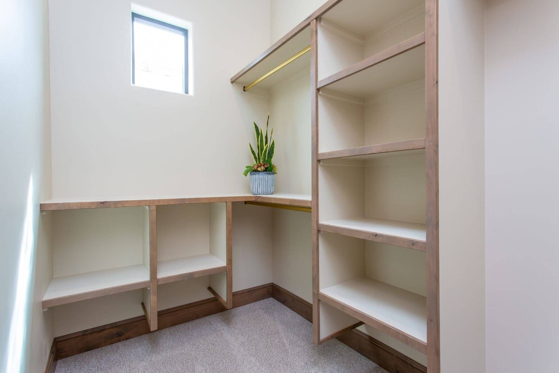 Empty, built-in shelves and desk area in a cream-colored closet, with a small plant on the desk.