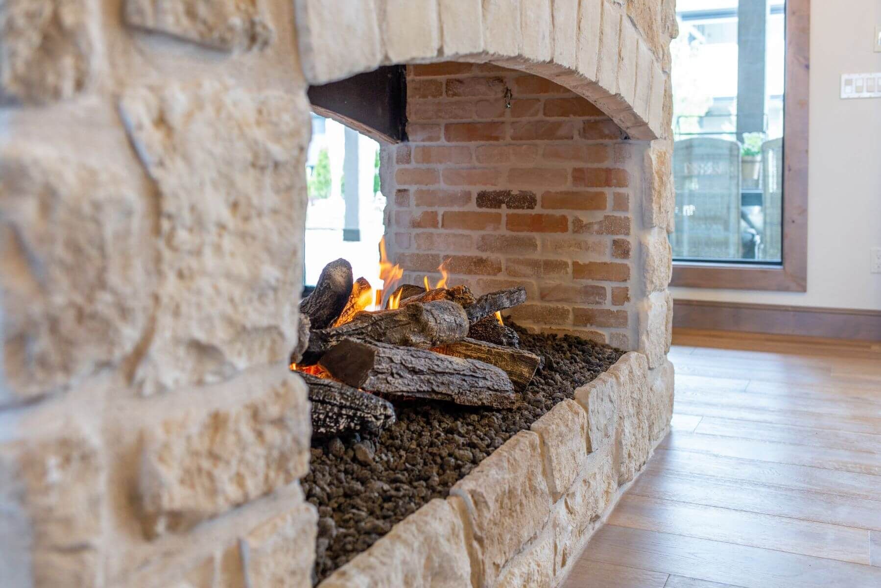 Fireplace with burning flames, brick and stone facade, modern interior.