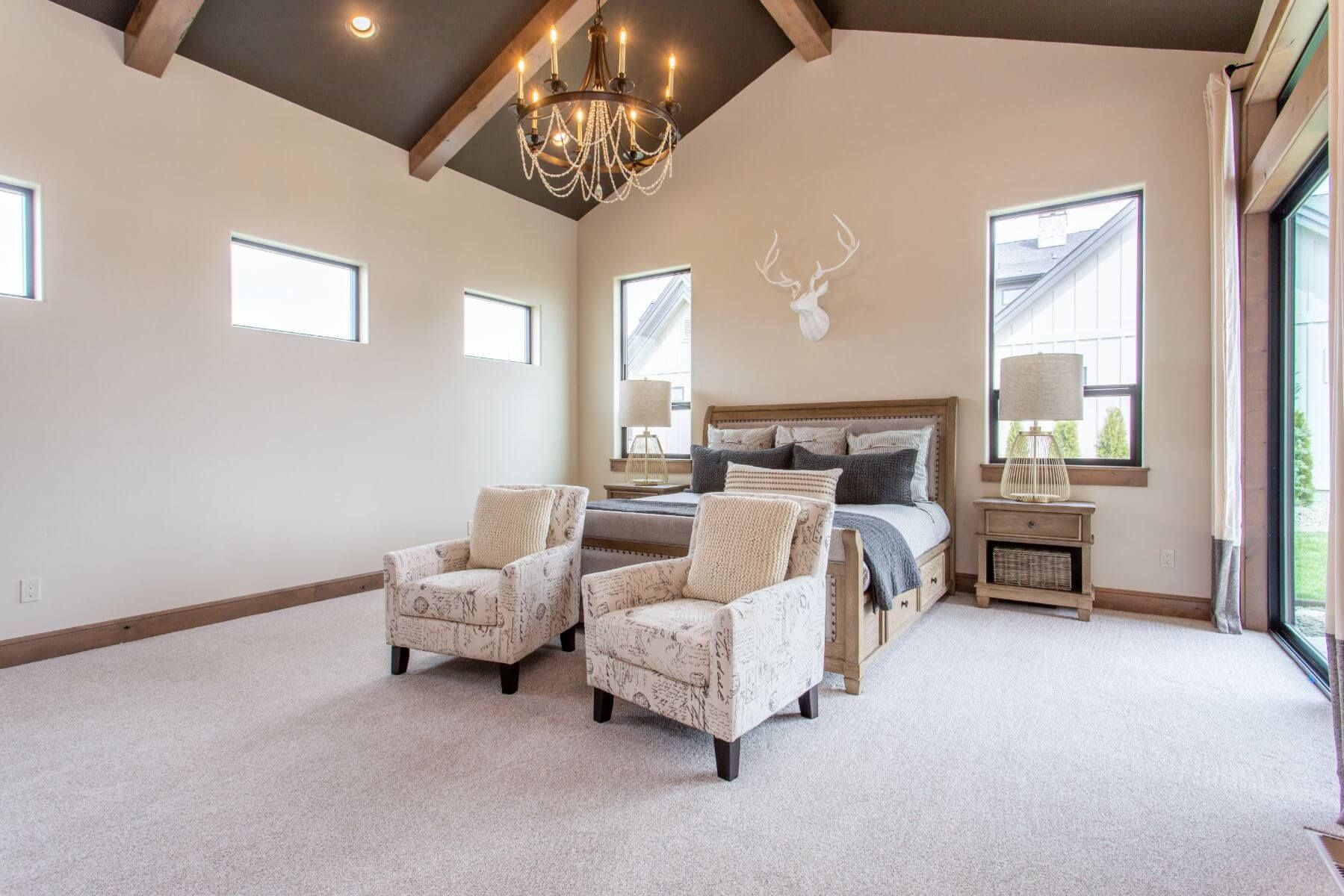 Spacious bedroom with high ceiling, crystal chandelier, two patterned armchairs, and a wooden bed.