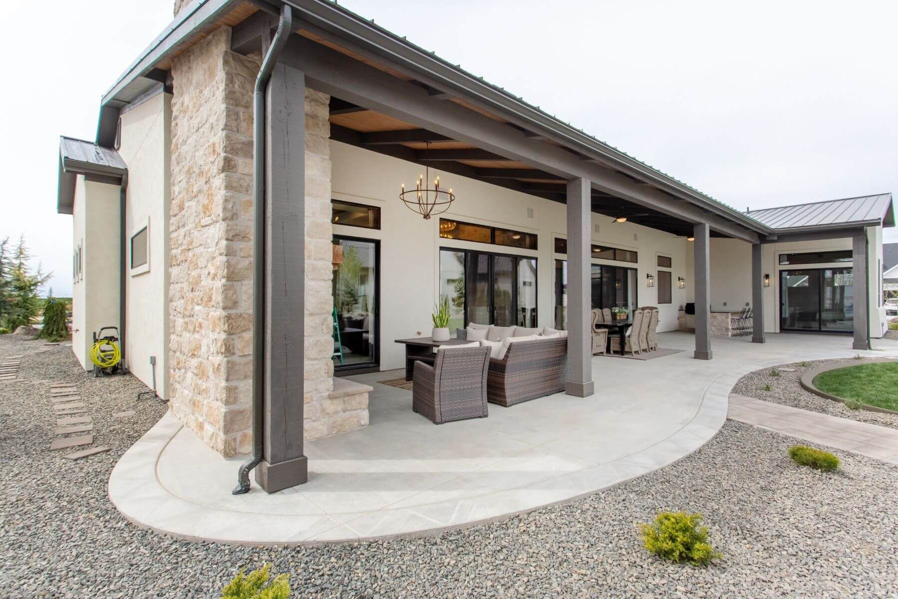 Covered patio with seating, neutral-toned exterior, stone accents, and gravel landscaping.