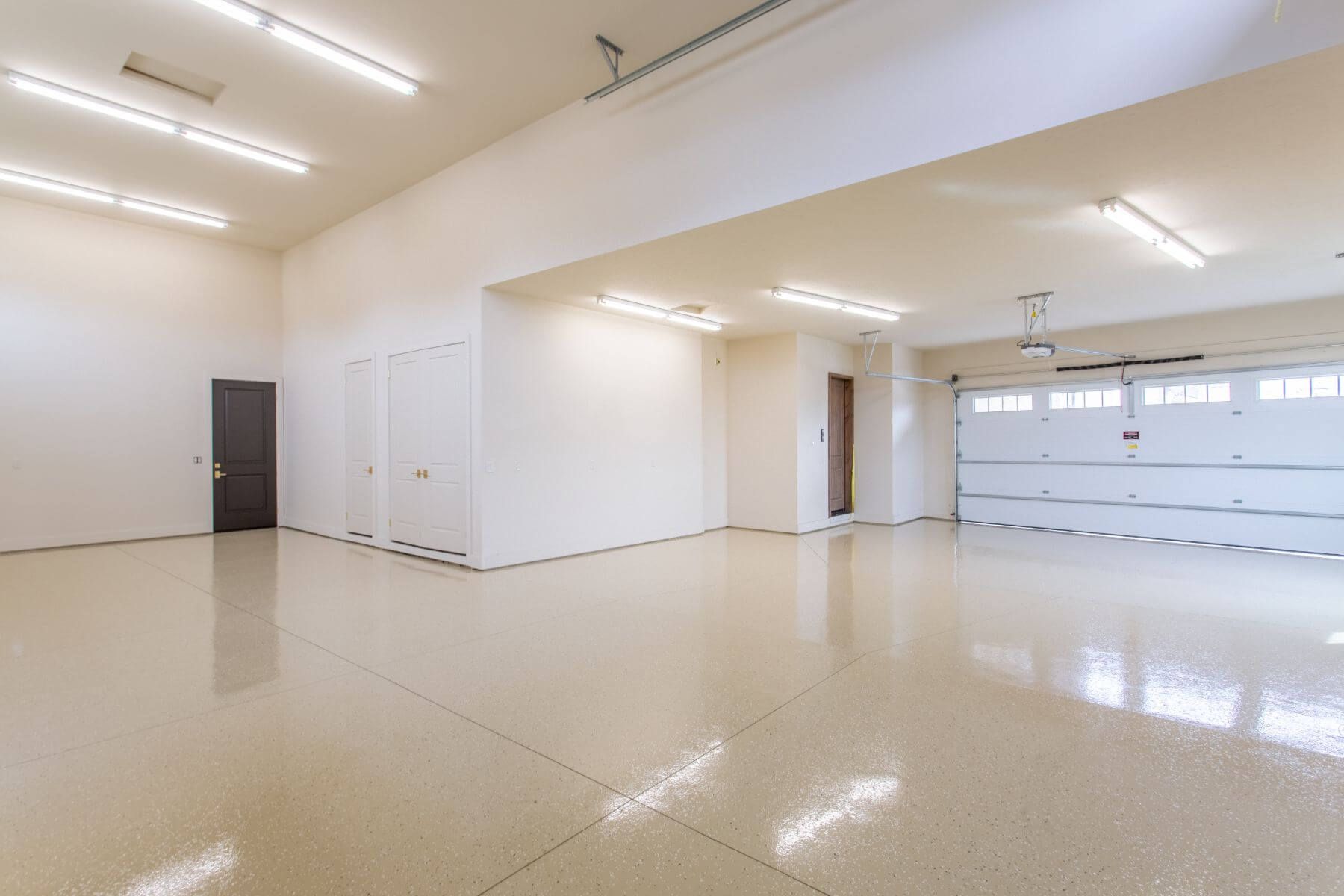 Empty, bright garage with epoxy floor. White walls, overhead lights, three doors, and garage door.