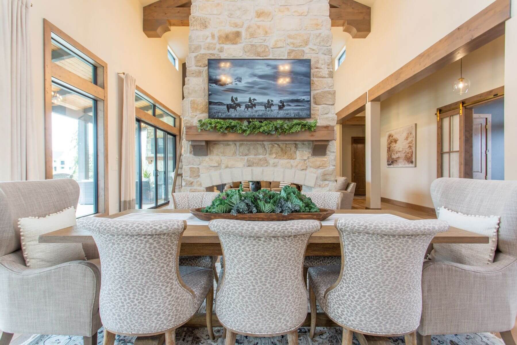 Dining room with stone fireplace, TV, wood table, and beige upholstered chairs.