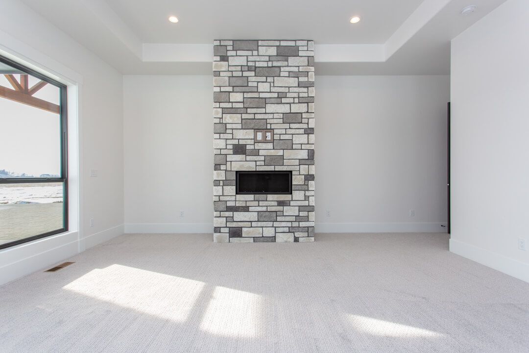 An empty living room with a stone fireplace and a flat screen tv.