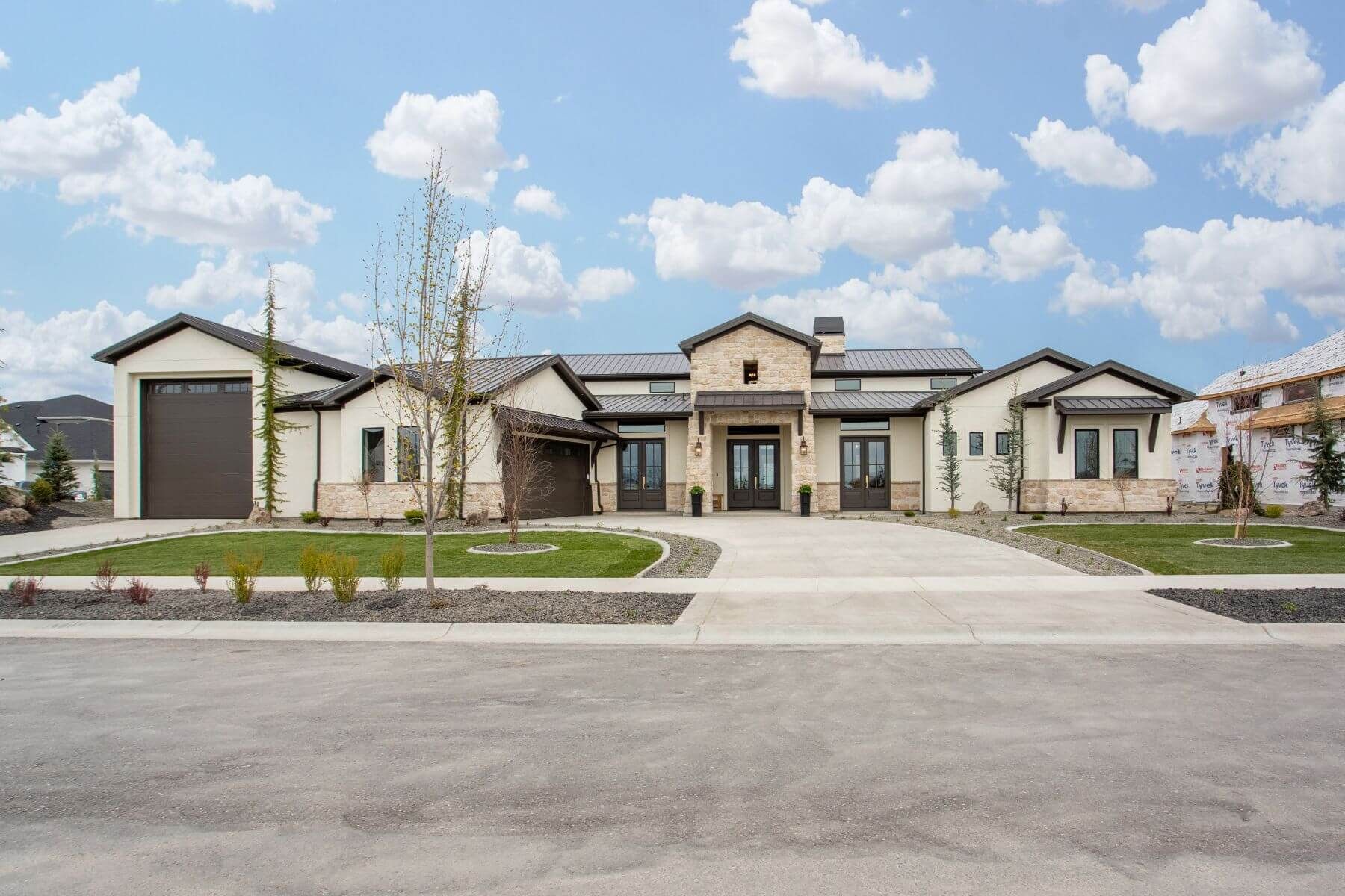 Modern, beige house with dark roof and garage, blue sky with clouds; driveway in front.