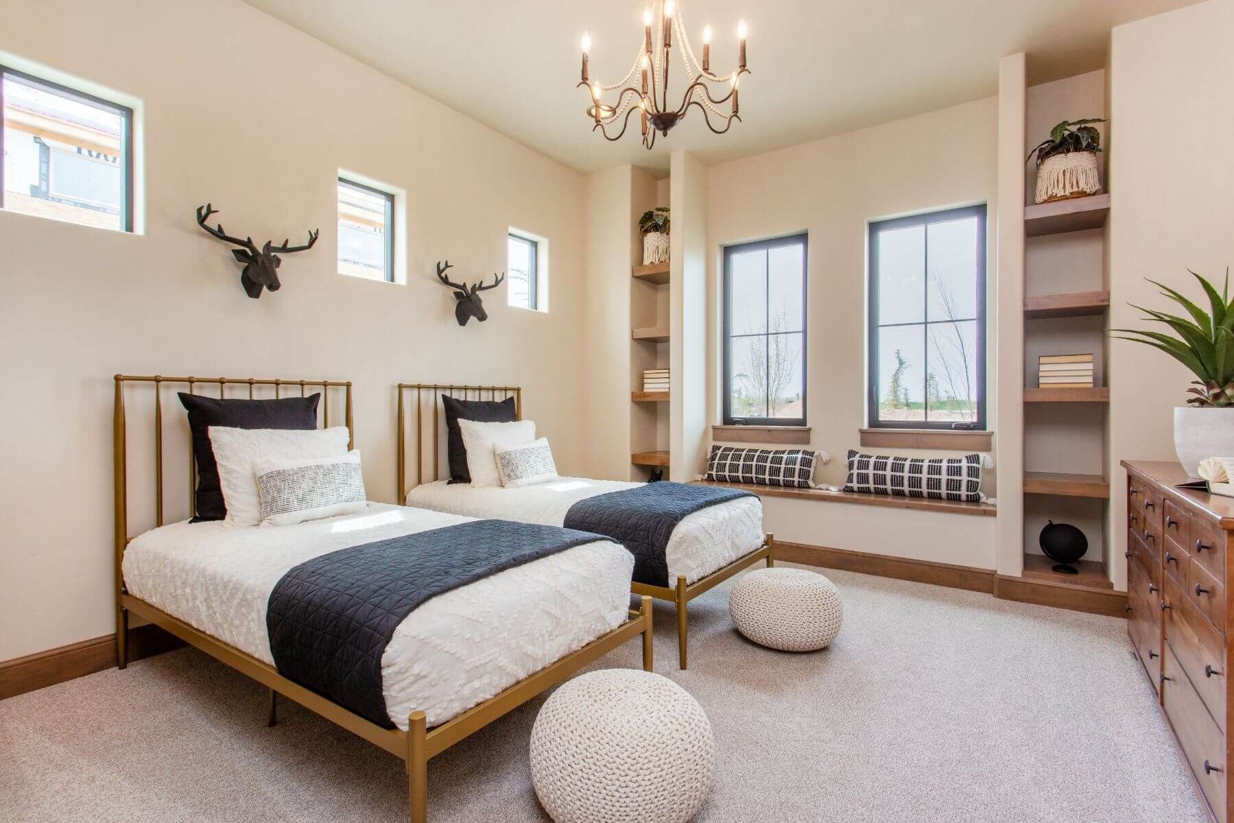 Bedroom with two twin beds, neutral tones, antlers, built-in shelving, and ottoman seating.