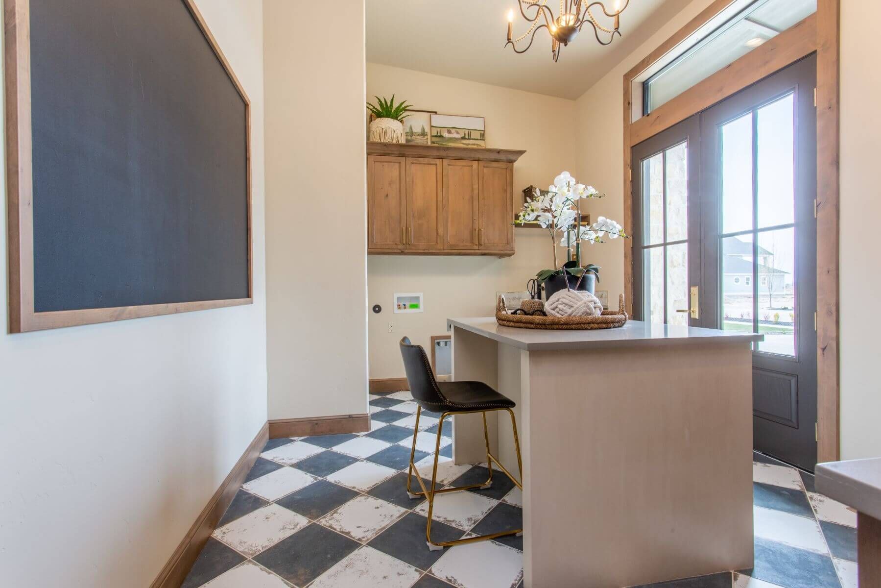 Laundry room with checkered floor, counter with stools, cabinets, chalkboard, and exterior door.