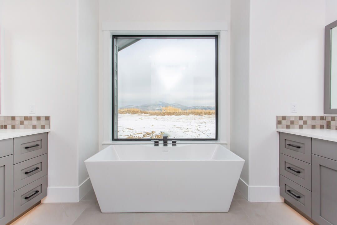 A bathroom with two sinks , a tub and a window.