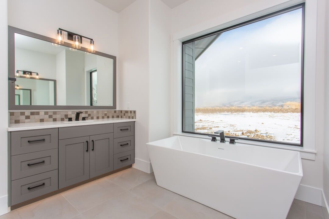 A bathroom with a tub , mirrors , and a large window.