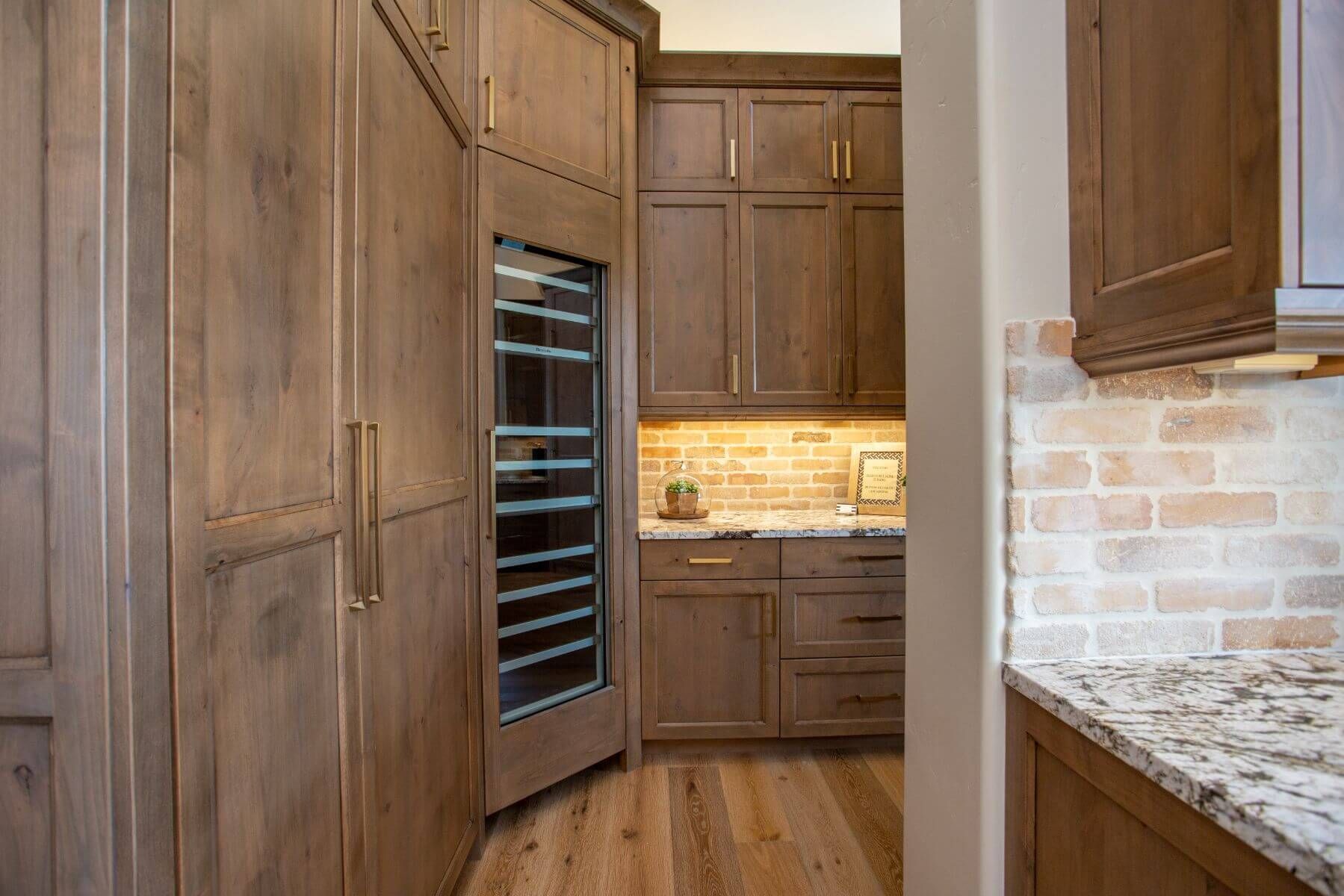 Wooden kitchen with built-in wine cooler, cabinets, and a granite countertop with brick backsplash.