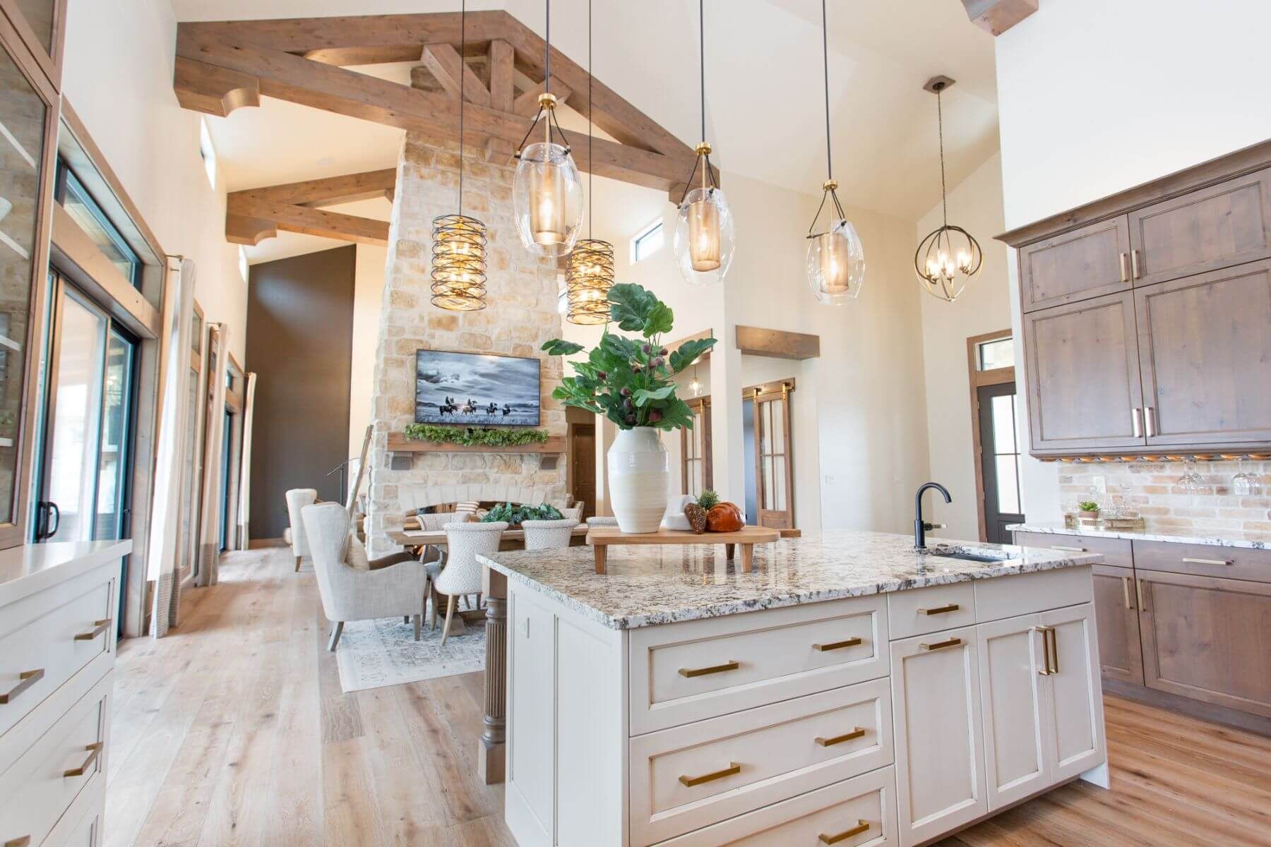 Spacious kitchen with island, rustic wood beams, stone fireplace, and light wood cabinets.