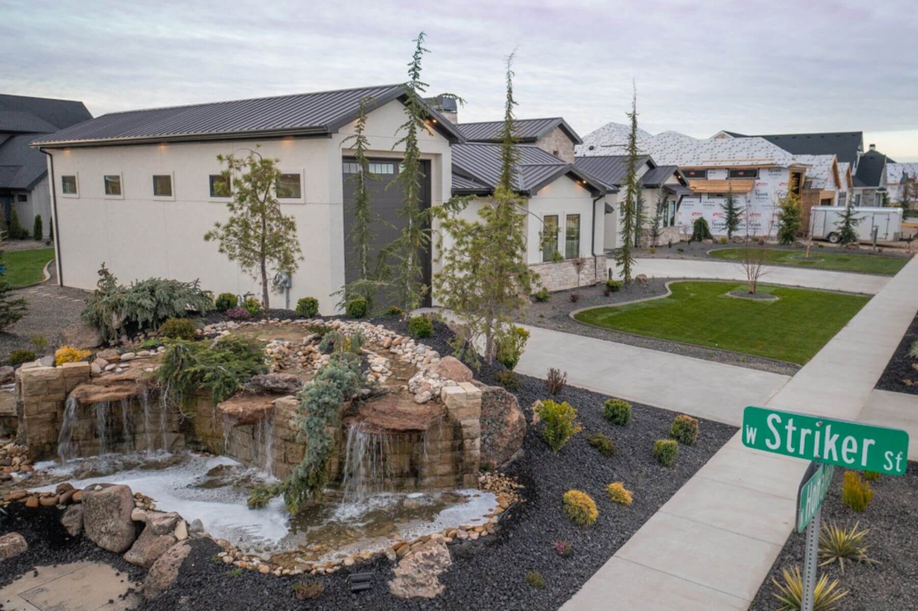 Modern home with a waterfall feature on a corner lot, green street sign, and cloudy sky.