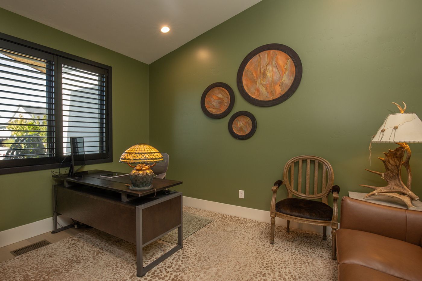 A home office with green walls , a desk , chair and lamp.
