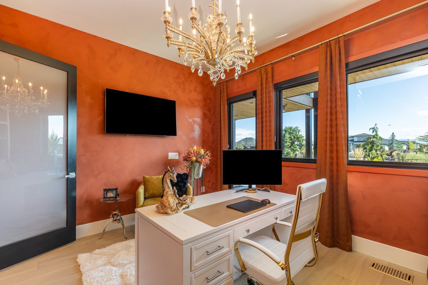A home office with a desk , chair , television and chandelier.