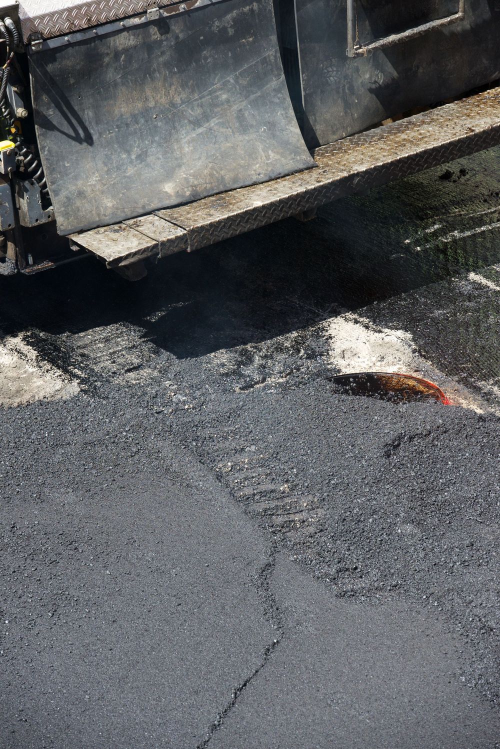 Macchina per la pavimentazione stradale che stende asfalto nero fresco sulla superficie di una strada.