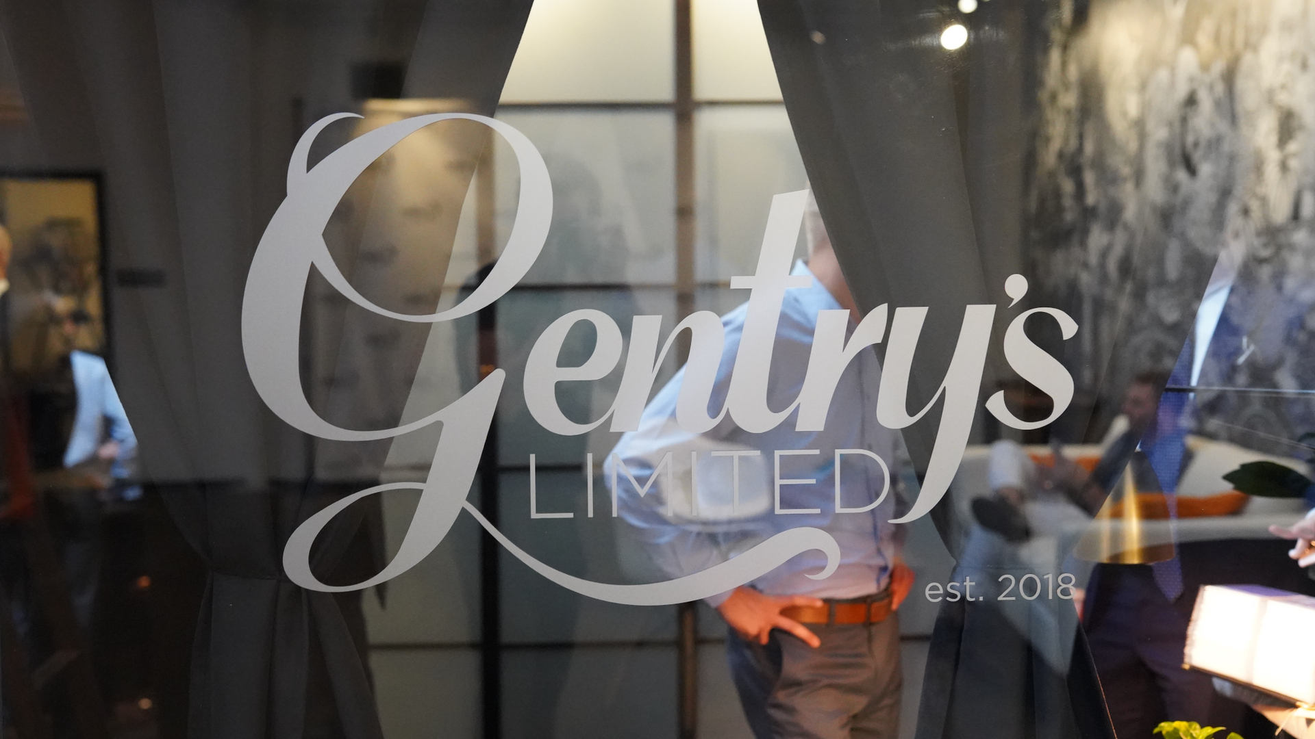 Two people chatting behind a glass door with “Gentry’s” lettering in a dimly lit venue.