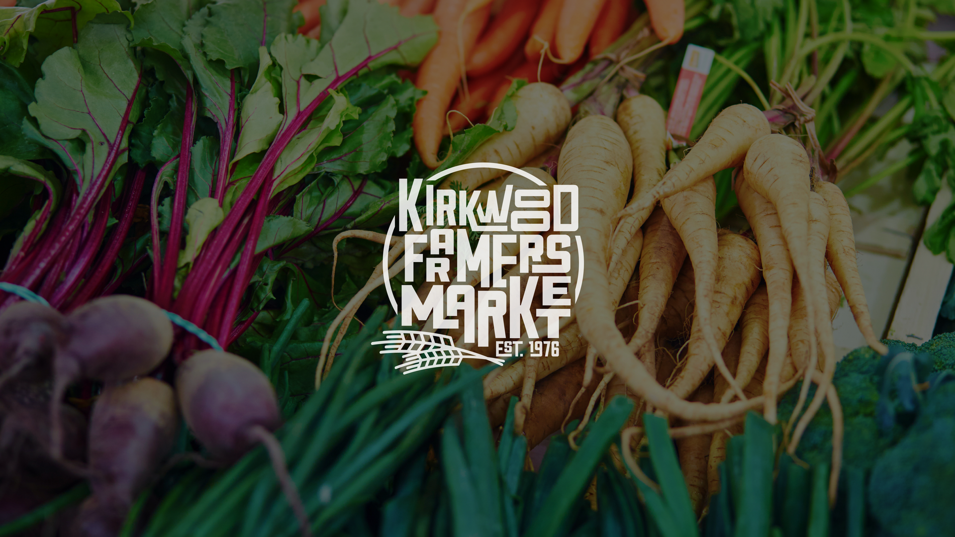 Kiaweo Farmers Market logo over colorful fresh vegetables and roots at a produce stall