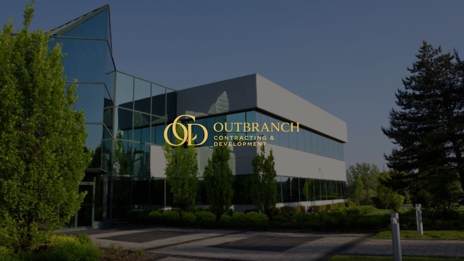 Modern glass office building with gold logo, surrounded by trees and greenery