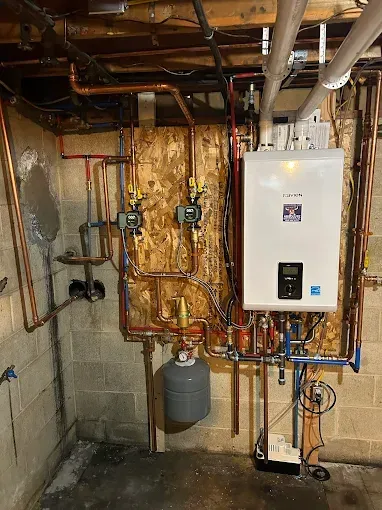 Basement utility room with boiler, pipes, gauges, and water heater mounted on unfinished concrete wall