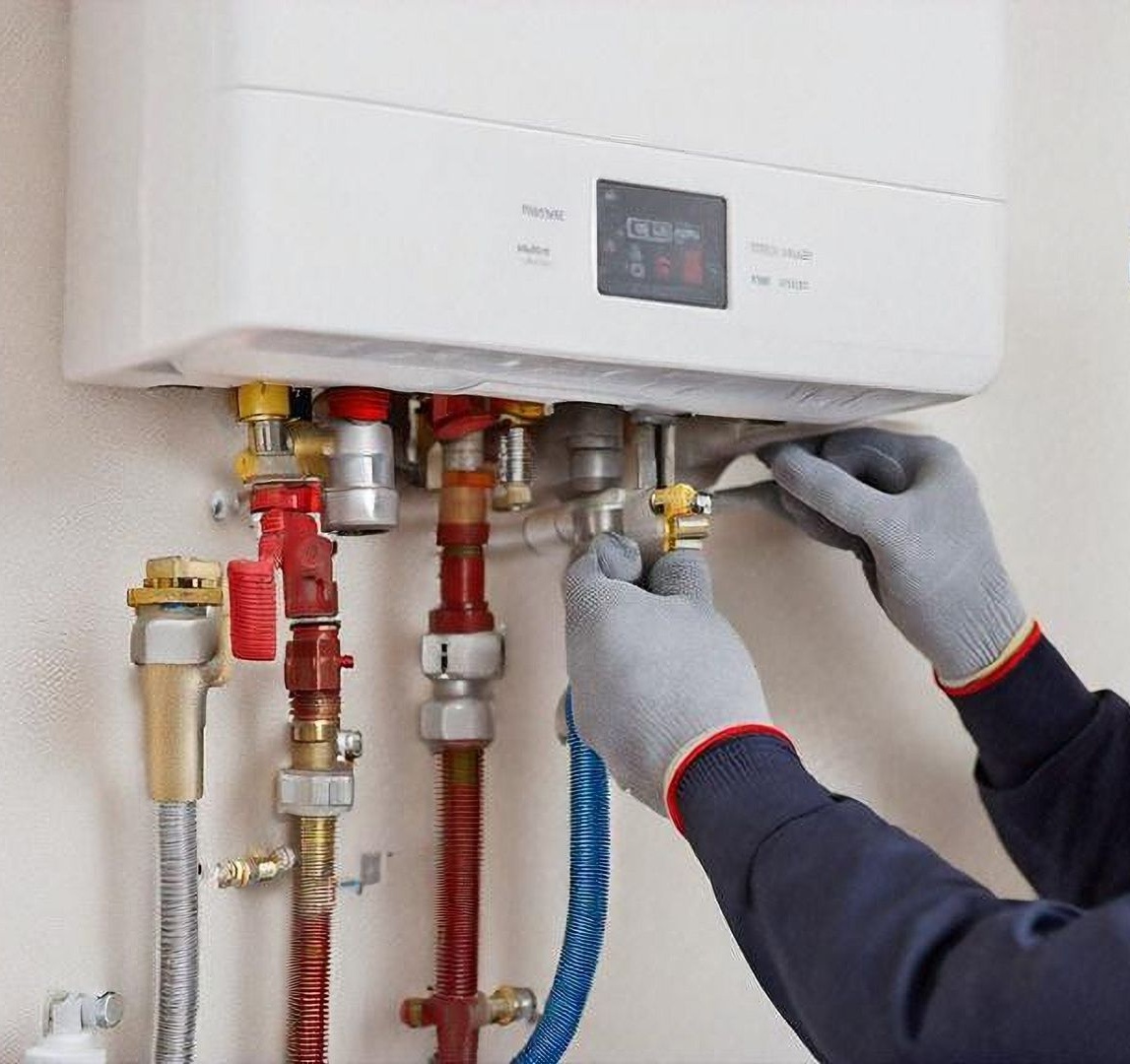 A technician wearing gray work gloves performs maintenance on the plumbing connections of a wall-mounted boiler.