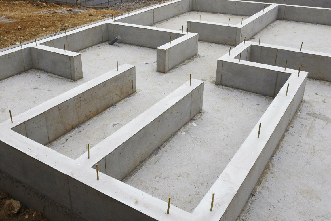 Concrete foundation walls forming a maze-like floor plan with wooden stakes on a construction site.