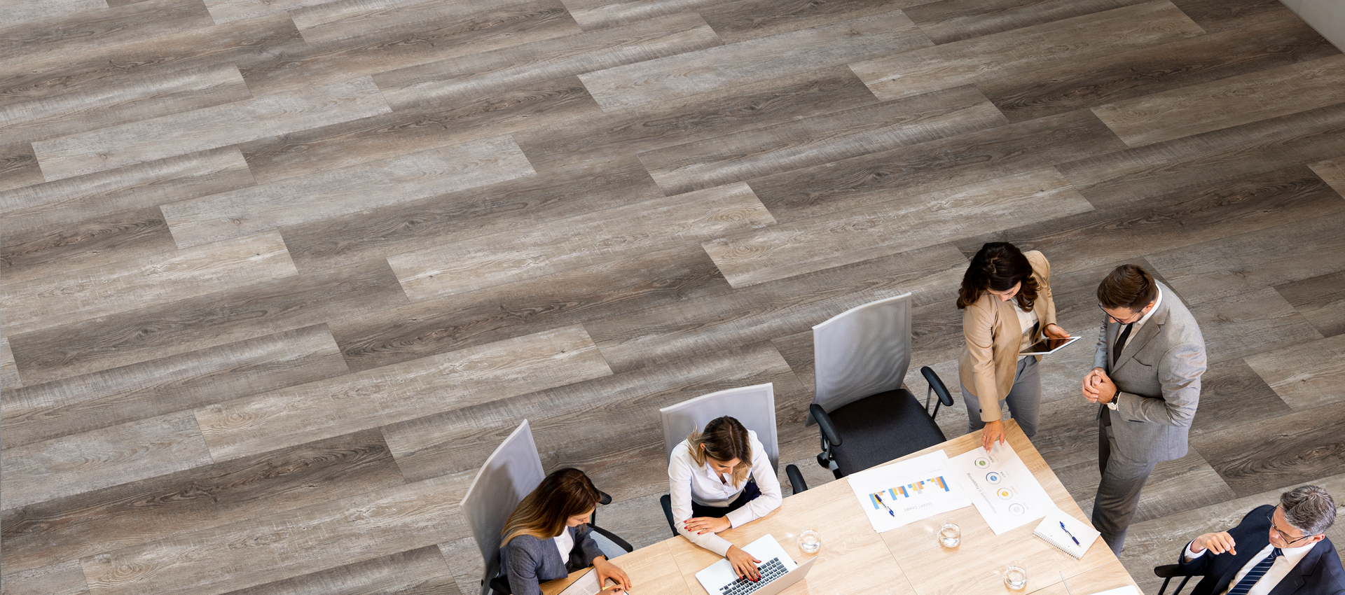 People gathered around a large table in a bright office, reviewing papers and discussing together.