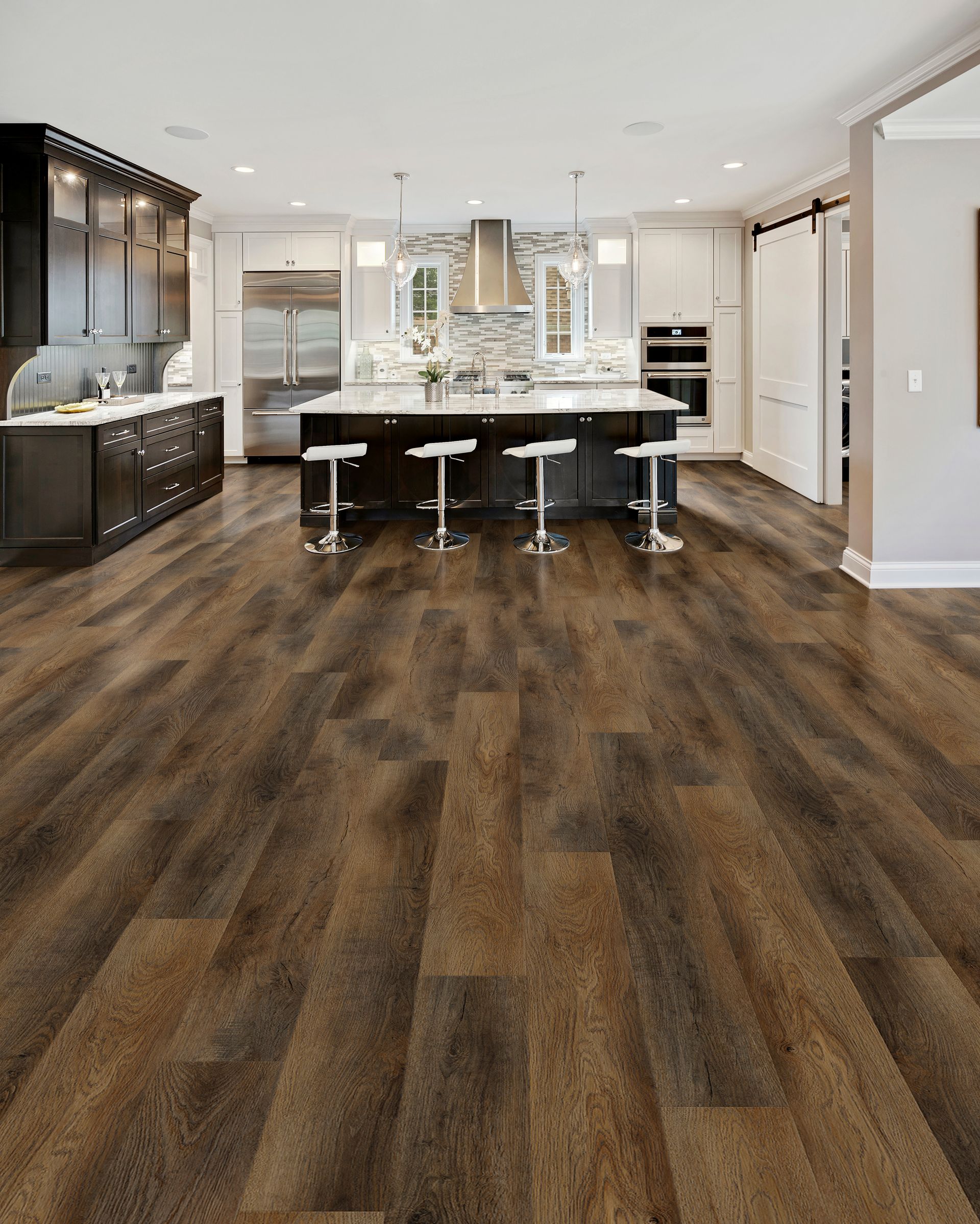 Modern open kitchen with dark wood floors, white cabinets, black island, and three stools